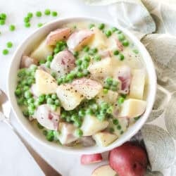 A bowl of creamed potatoes and peas next to a spoon and napkin.