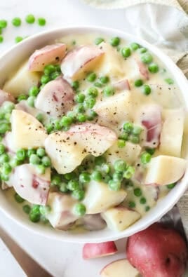 A bowl of creamed potatoes and peas next to a spoon and napkin.