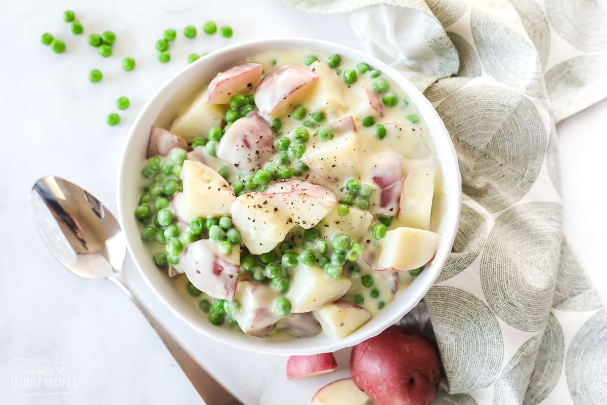 A bowl of creamed potatoes and peas next to a spoon and napkin.