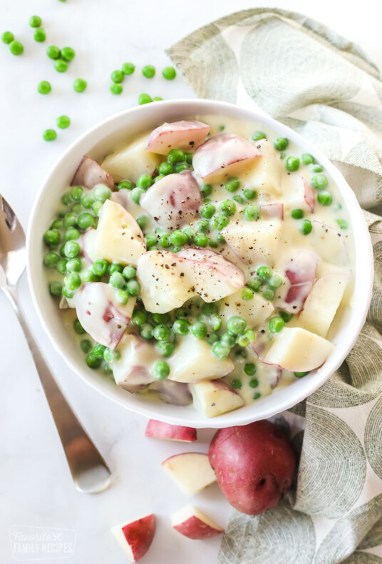 A top view of a bowl with cooked red potatoes and peas in a cream sauce.
