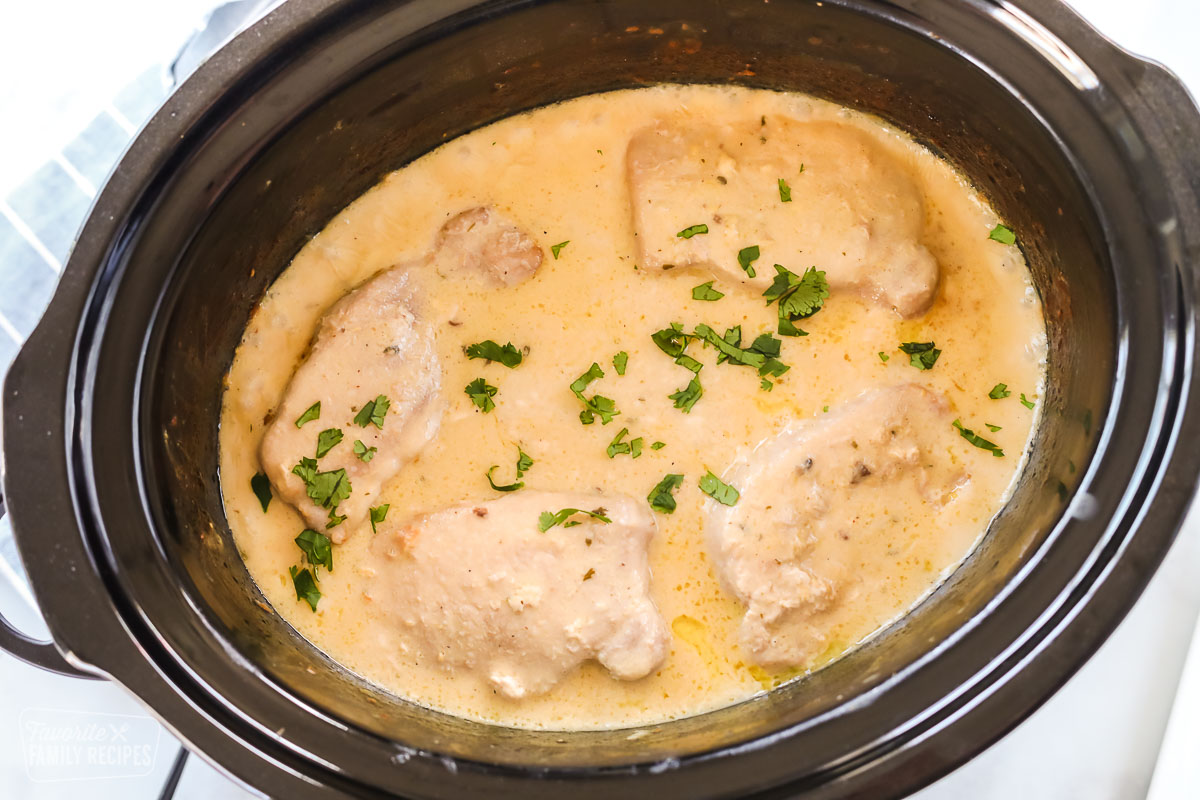 Pork chops in a creamy sauce in a Crock Pot with parsley sprinkled over the top.
