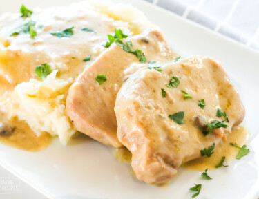 Pork chops made in a crock pot and mashed potatoes with gravy on a plate.