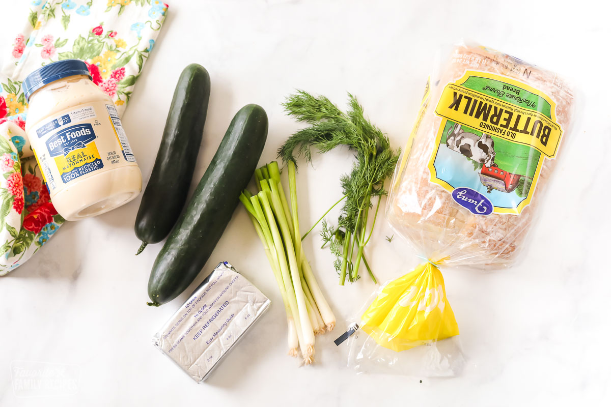 Ingredients to make cucumber sandwiches including bread, cucumbers, cream cheese, green onion, mayo, and dill