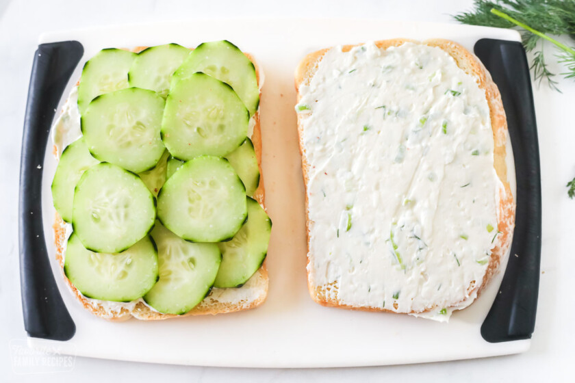 A slice of bread with a cream cheese spread and another slice of bread with sliced cucumbers