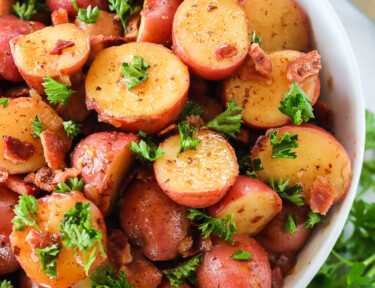 German potato salad made with red potatoes, vinegar, onion, bacon, and parsley in a bowl.