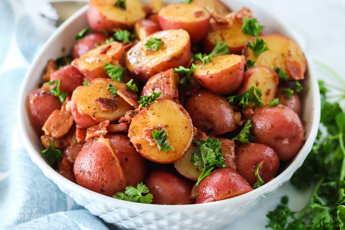 A bowl of halved red potatoes with a bacon vinegar glaze, garnished with parsley and bacon bits combined to make German Potato Salad.