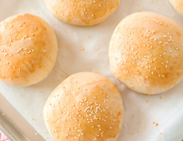 A baking sheet with six hamburger buns that have been freshly baked