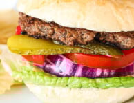 A hamburger on a plate with pickles, lettuce, tomato, and red onion and a side of wavy potato chips