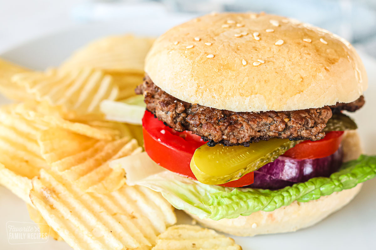 A hamburger with pickles, tomatoes, lettuce, and onion on a plate with ruffled potato chips.
