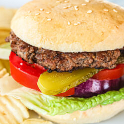 A close up of a hamburger with lettuce, tomatoes, pickles, and onion.