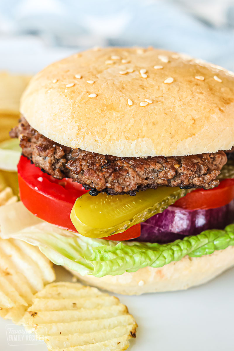 A close up of a hamburger with lettuce, tomatoes, pickles, and onion.