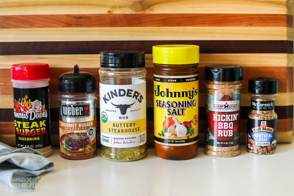 Six different hamburger seasonings lined up in front of a cutting board.