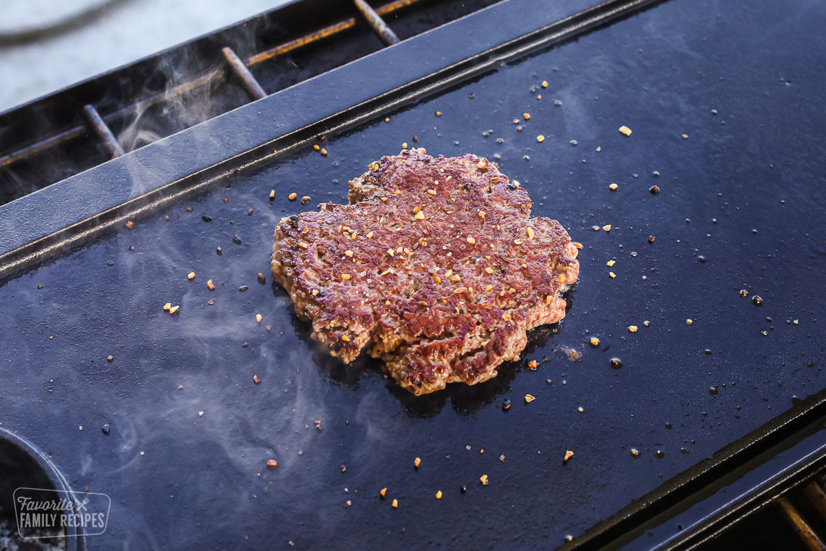 A hamburger patty cooking on the grill with seasonings on top