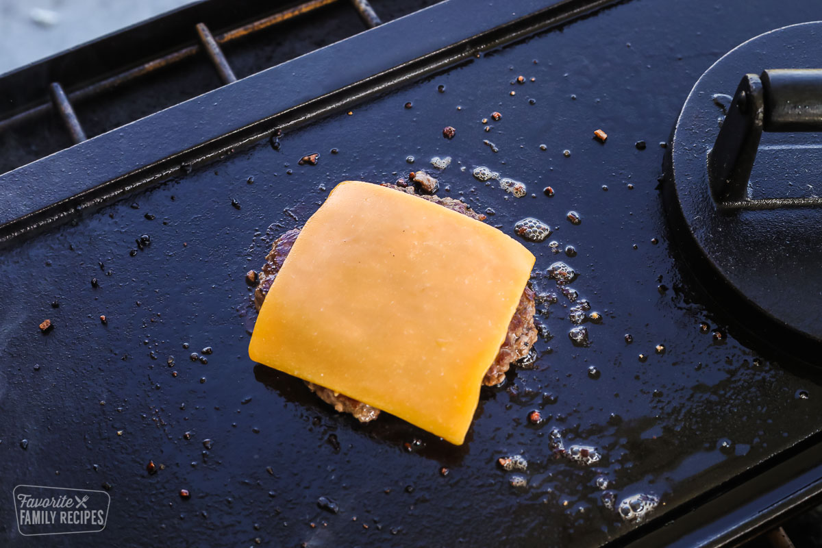 A hamburger patty on the grill with a slice of cheese over the top