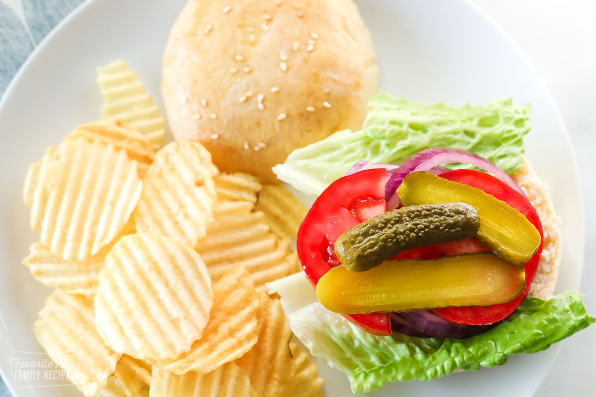 An open faced hamburger bun with lettuce, tomato, onions, and pickles on a plate