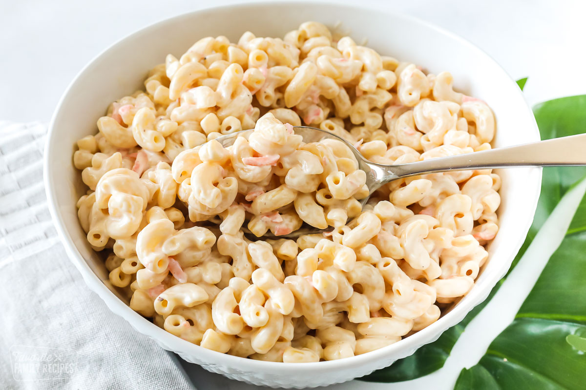 A spoon taking a scoop of Hawaiian macaroni salad from a serving bowl.