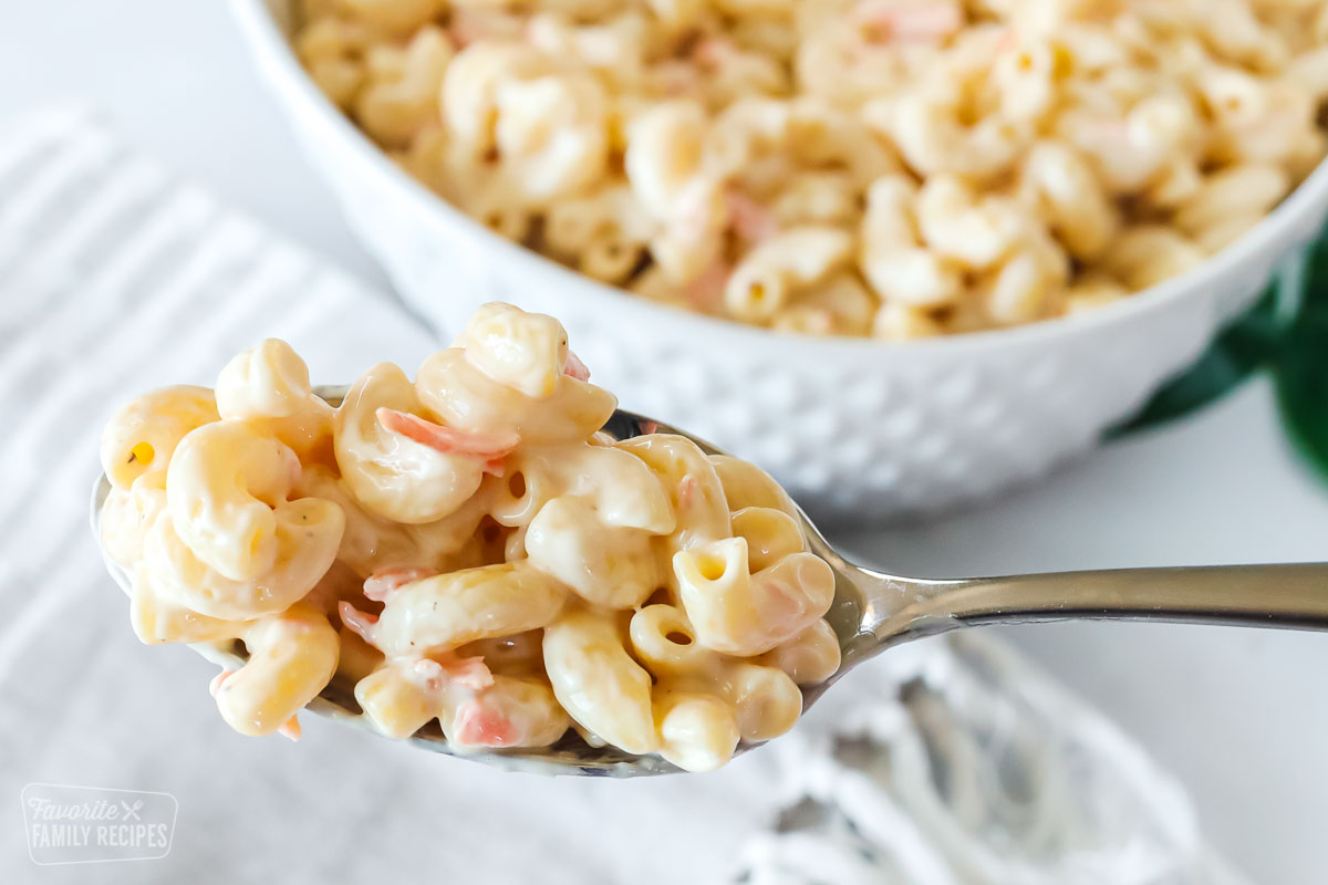 Close up of Hawaiian macaroni salad on a serving spoon to show the detail of the macaroni noodles, carrot, and dressing.