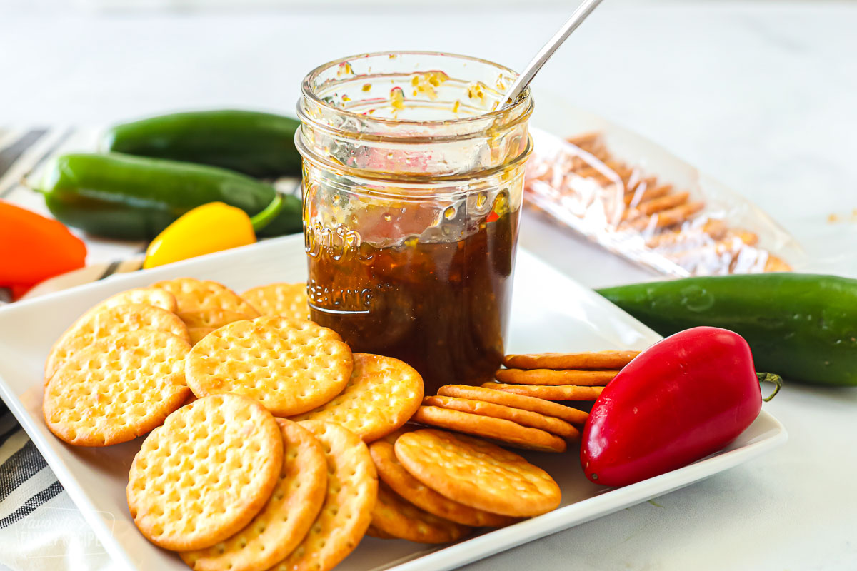 A jar of jalapeño jelly and a plate of crackers next to some small fresh peppers