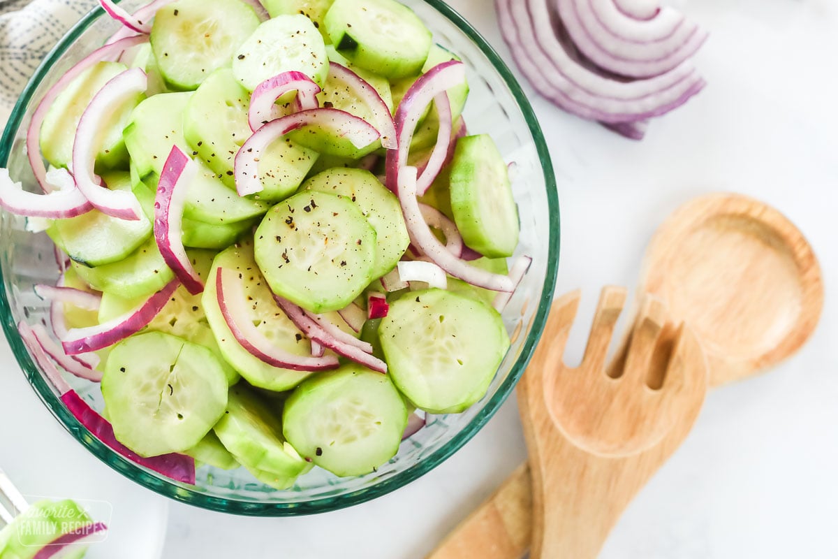 Cucumber Vinegar Salad with red onion slices n a large glass bowl with serving spoons on the side.