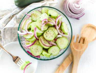 Cucumber salad with marinated cucumbers in a bowl and a plate with a fork holding a bite-sized piece