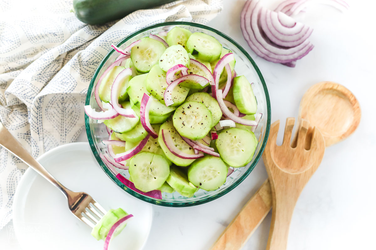 Cucumber salad with marinated cucumbers in a bowl and a plate with a fork holding a bite-sized piece