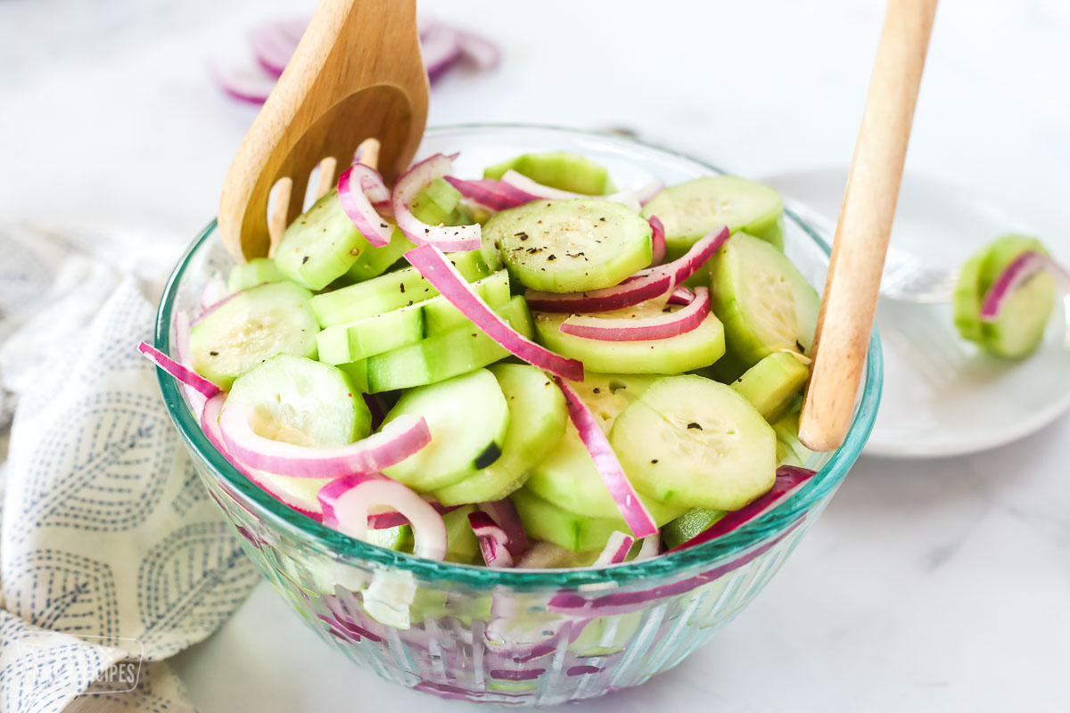 Marinated Cucumber Salad in a clear glass bowl with wooden serving spoons