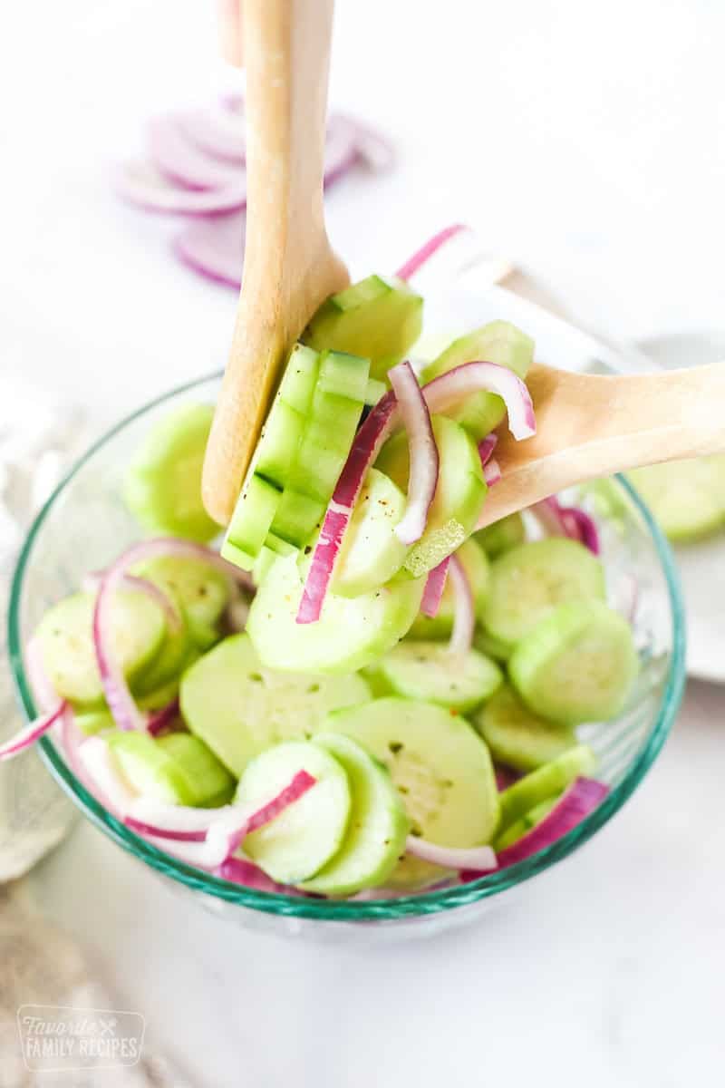 Cucumber salad being pulled up from a bowl with wooden salad spoons