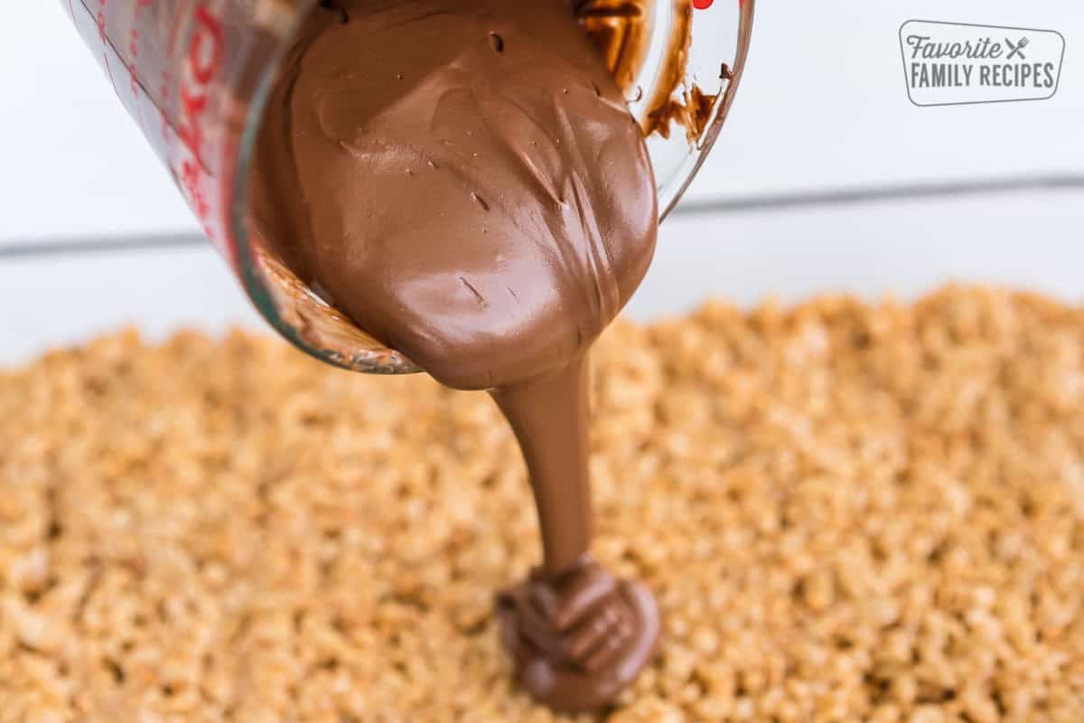 These no-bake Scotcharoos, also known as Oh Henry Bars, are a favorite treat. A Rice Krispie and peanut butter center is covered with a chocolate butterscotch topping. Chocolate being poured onto a Scotcharoo base.
