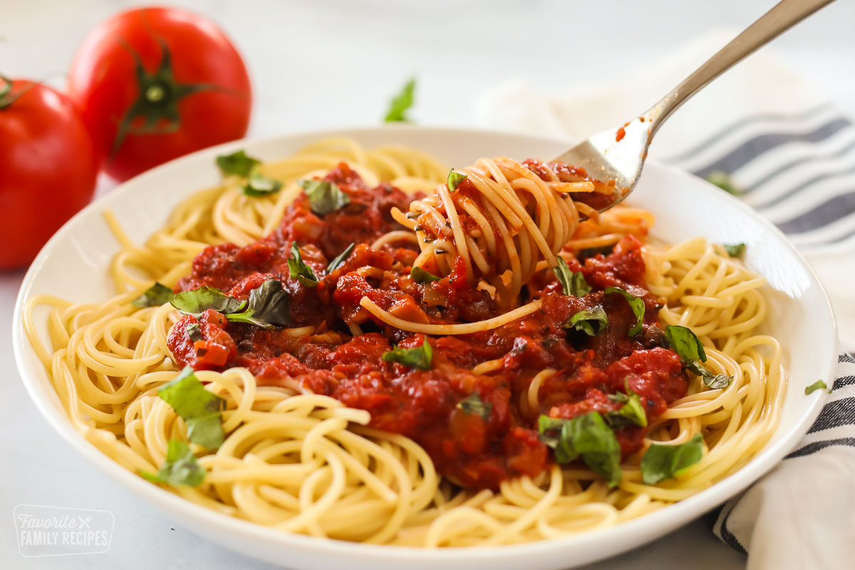 A bowl of spaghetti with marinara sauce with the pasta twirled around a fork.