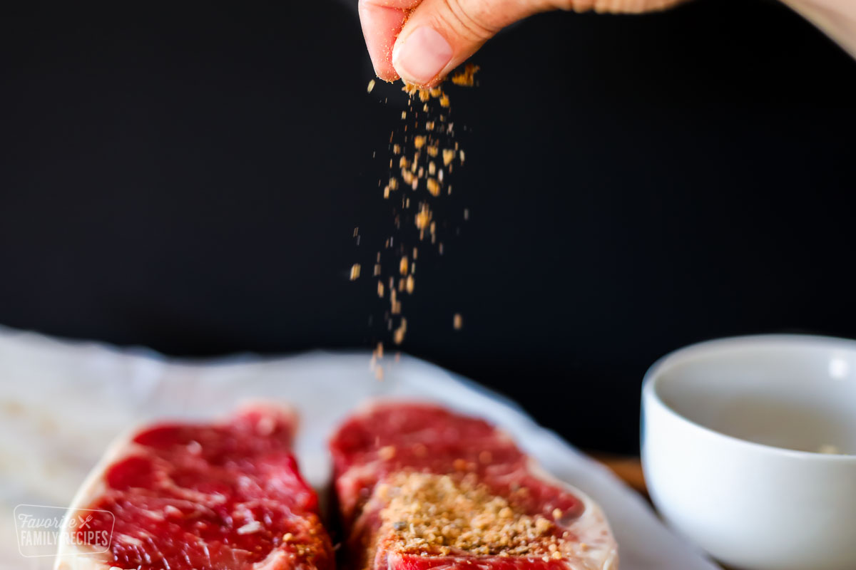 Dry rub being sprinkled onto a cut of uncooked steak.