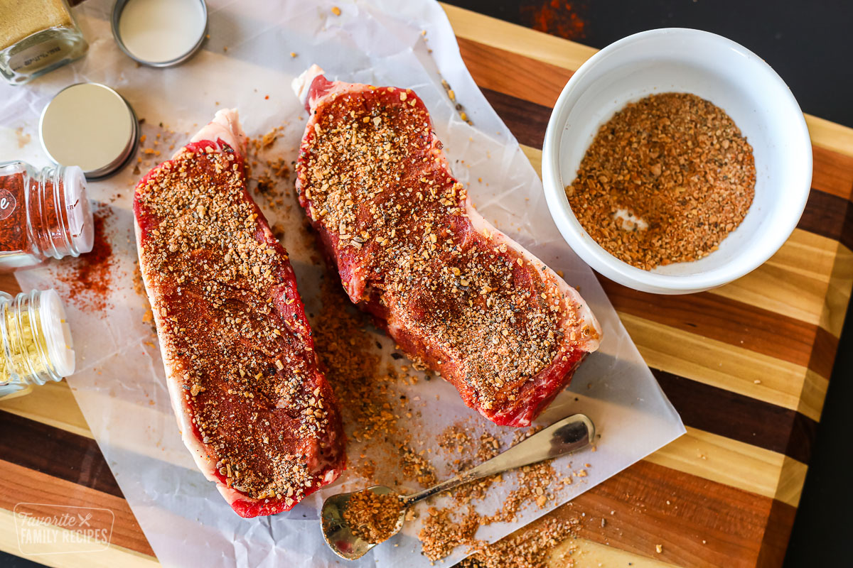 Two seasoned uncooked steaks with a bowl of dry rub next to them.