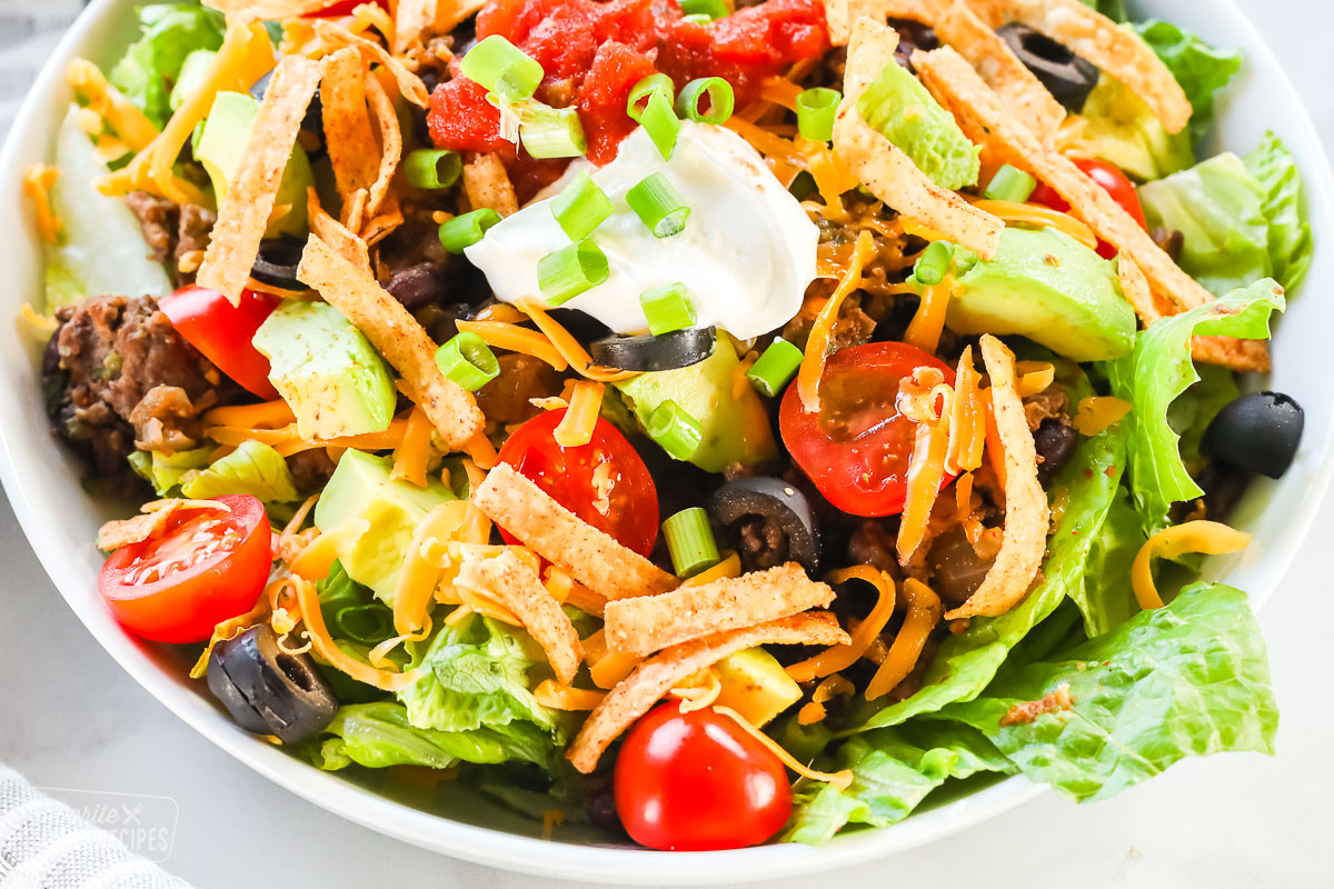 A close up view of a taco salad bowl with ground beef and taco toppings.