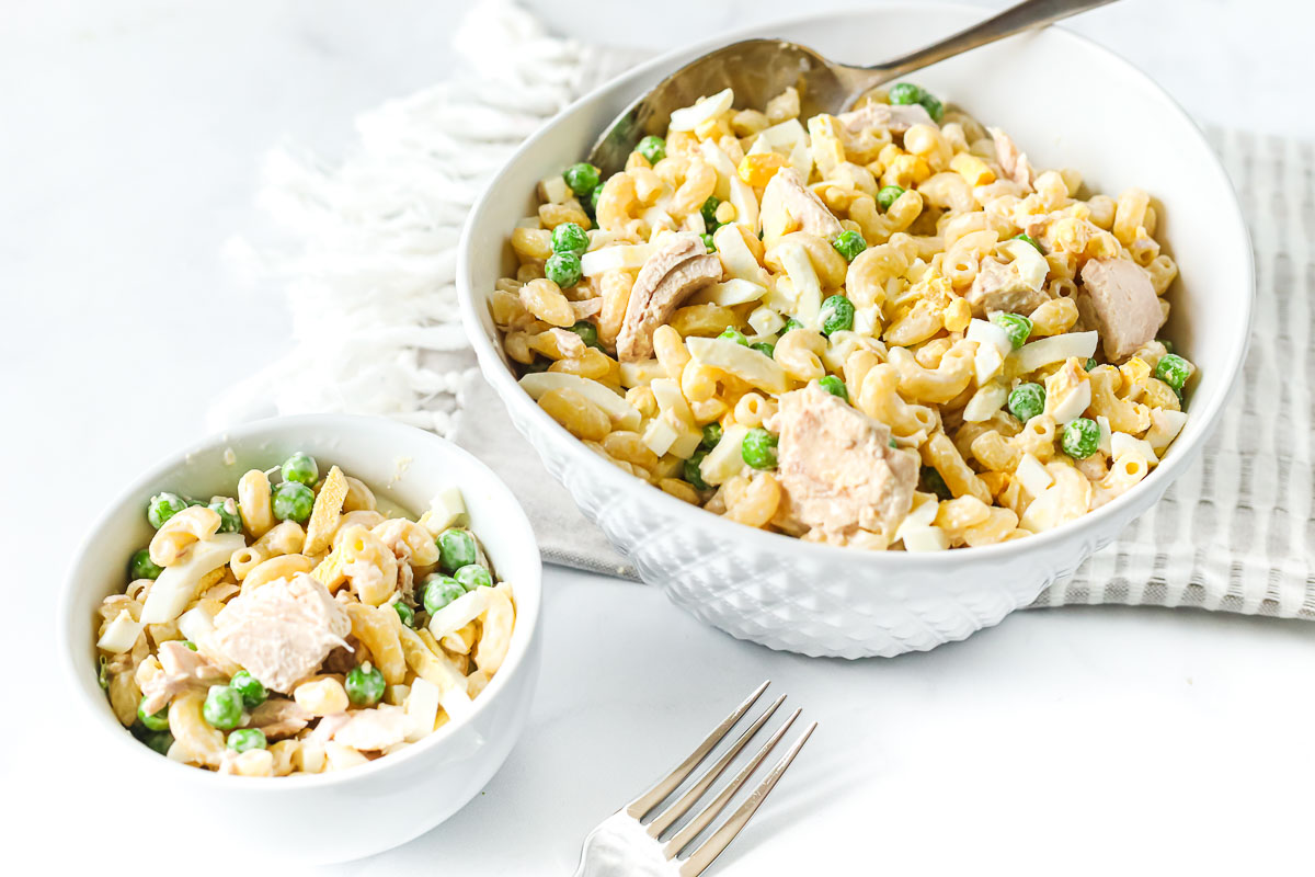 A serving bowl of macaroni salad with tuna, hard boiled egg, and peas.