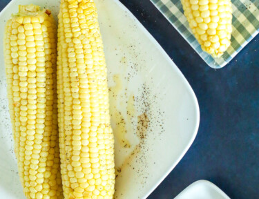 Cooked Air Fryer Corn on the Cob on 2 plates with a side of butter