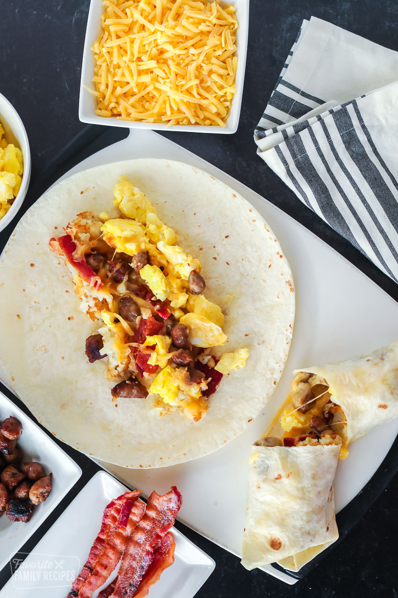 An open-faced breakfast burrito and a rolled breakfast burrito with eggs, sausage, bacon, cheese, and hash browns.
