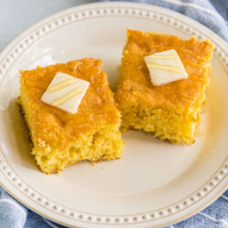 Two pieces of cornbread on a plate with butter and honey