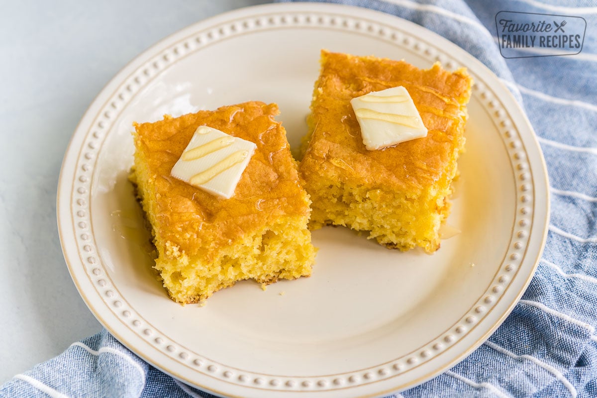 Two pieces of cornbread on a plate with butter and honey.