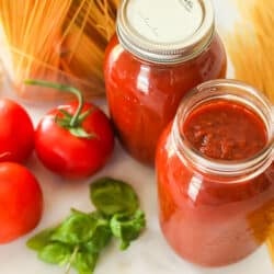 Two glass jars of canned spaghetti sauce next to dry spaghetti
