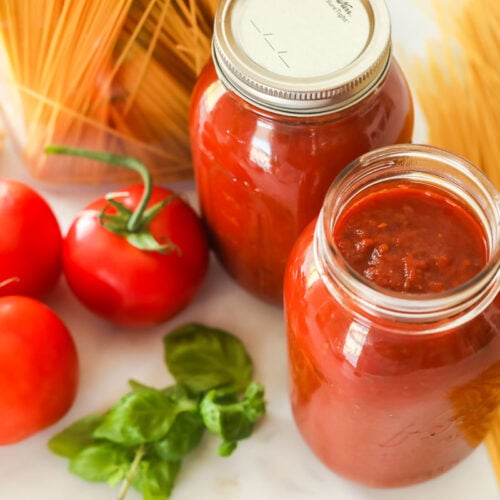 Two glass jars of canned spaghetti sauce next to dry spaghetti