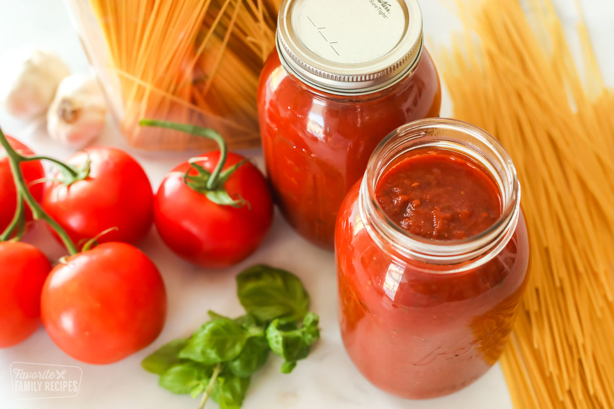 Two glass jars of canned spaghetti sauce next to dry spaghetti