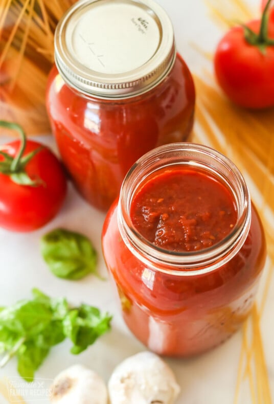 Spaghetti Sauce in glass canning jars next to tomatoes and basil