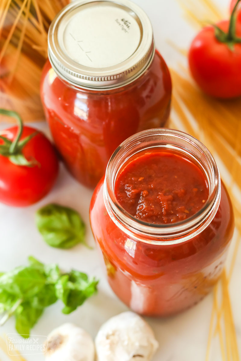 Spaghetti Sauce in glass canning jars next to tomatoes and basil