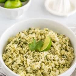 A bowl of cilantro lime rice next to a juicer and a bowl of lime