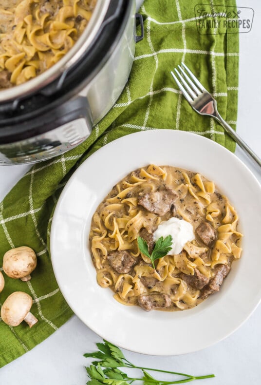 A bowl full of beef stroganoff topped with sour cream and parsley