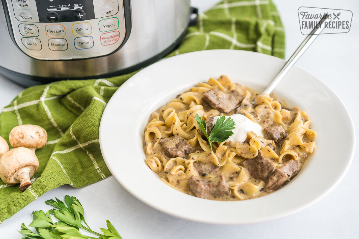 A bowl full of beef stroganoff topped with sour cream and parsley.