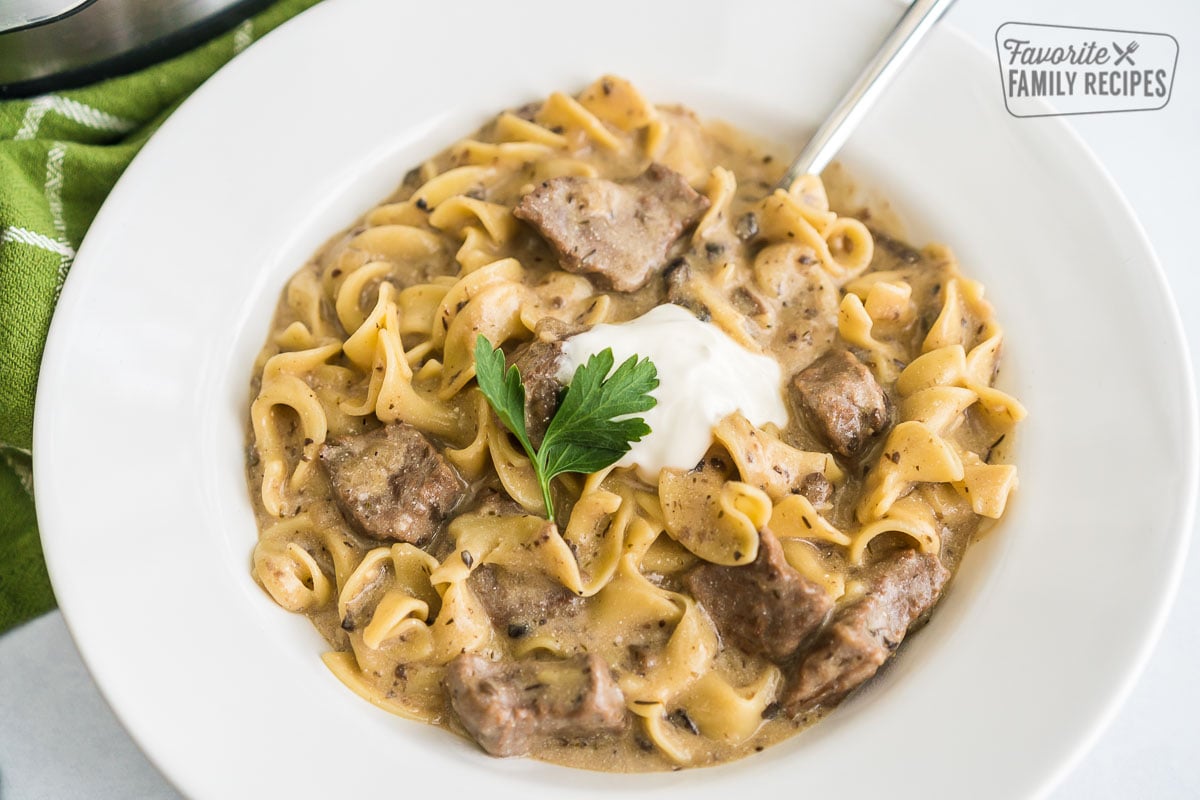 Egg noodles, beef, and sauce in a bowl topped with sour cream and parsley.