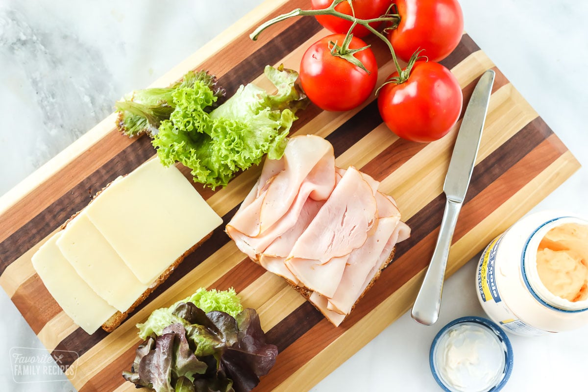 Slices of bread with turkey and cheese next to tomatoes and lettuce