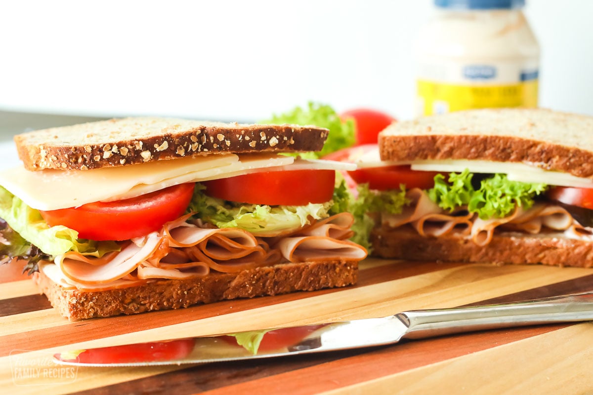 Two turkey sandwiches next to a jar of mayonnaise and a knife