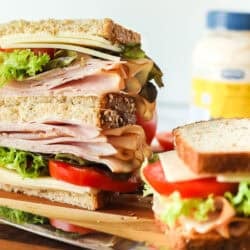 Deli turkey sandwich stacked on a cutting board next to another sandwich