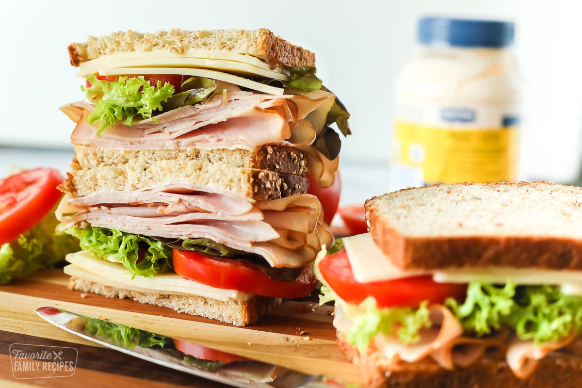 Deli turkey sandwich stacked on a cutting board next to another sandwich